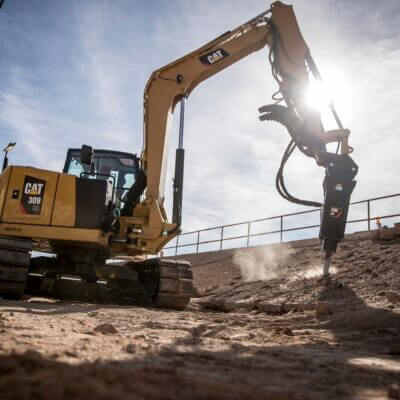 Escavatore Caterpillar a noleggio al lavoro con martello durante un lavoro di manutenzione del verde CGTE Vermietung:
